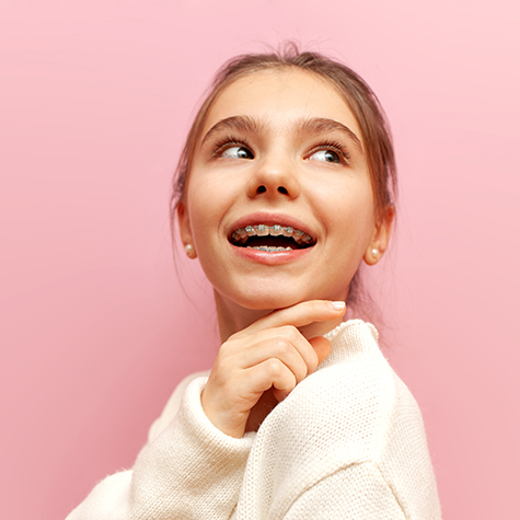 Cheerful young girl with metal braces smiling and looking up against a pink background